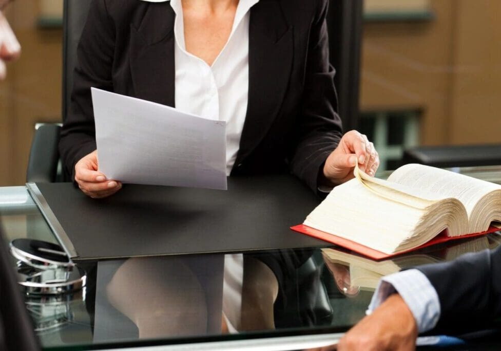 A woman is holding papers and sitting at a table.